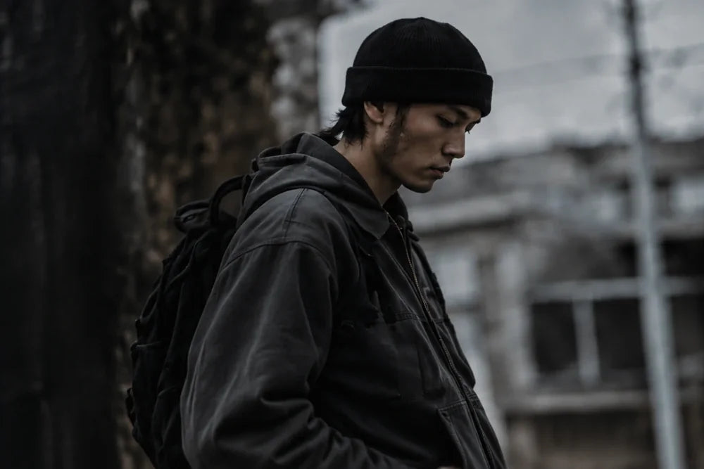A figure in a worn work jacket on a grey street