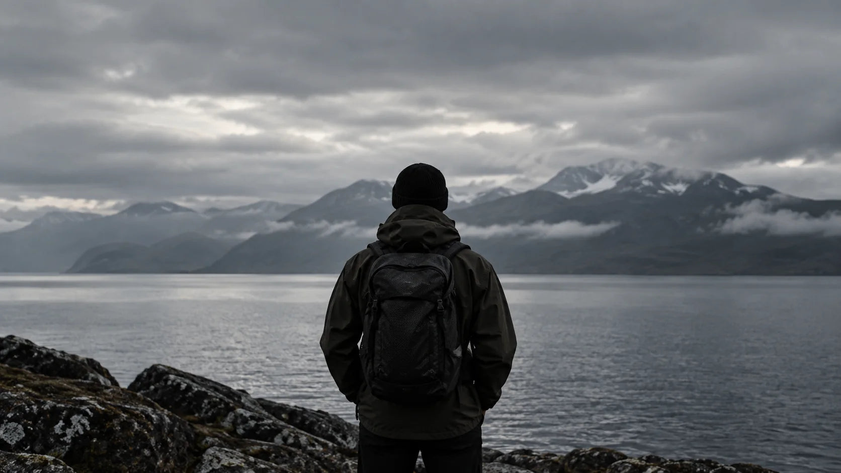A hiker looking across a grey fjord